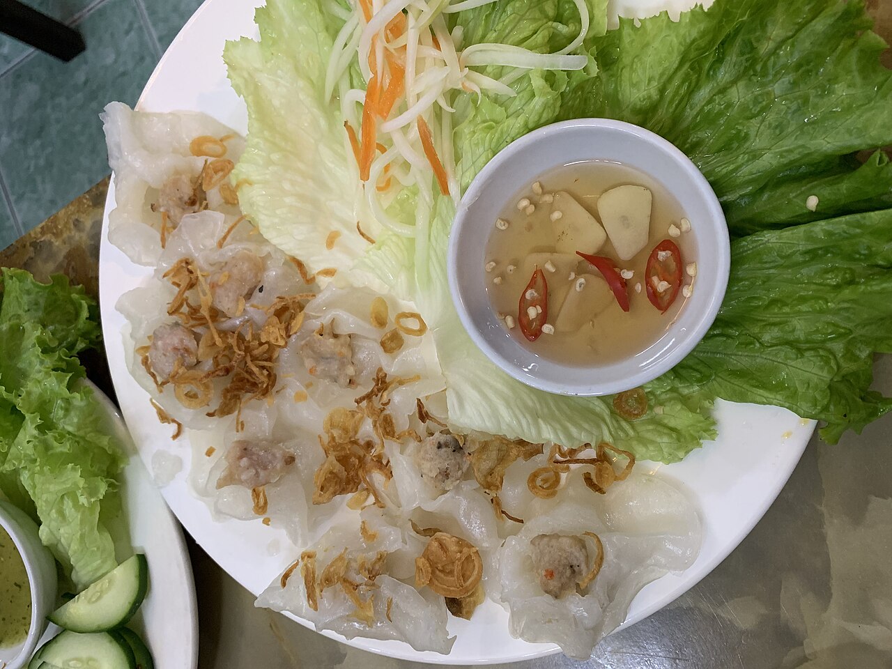 Đĩa bánh bao bánh vạc với hành phi rau và nước chấm minh họa câu hỏi về nhân dị ứng và tiếp xúc chéo