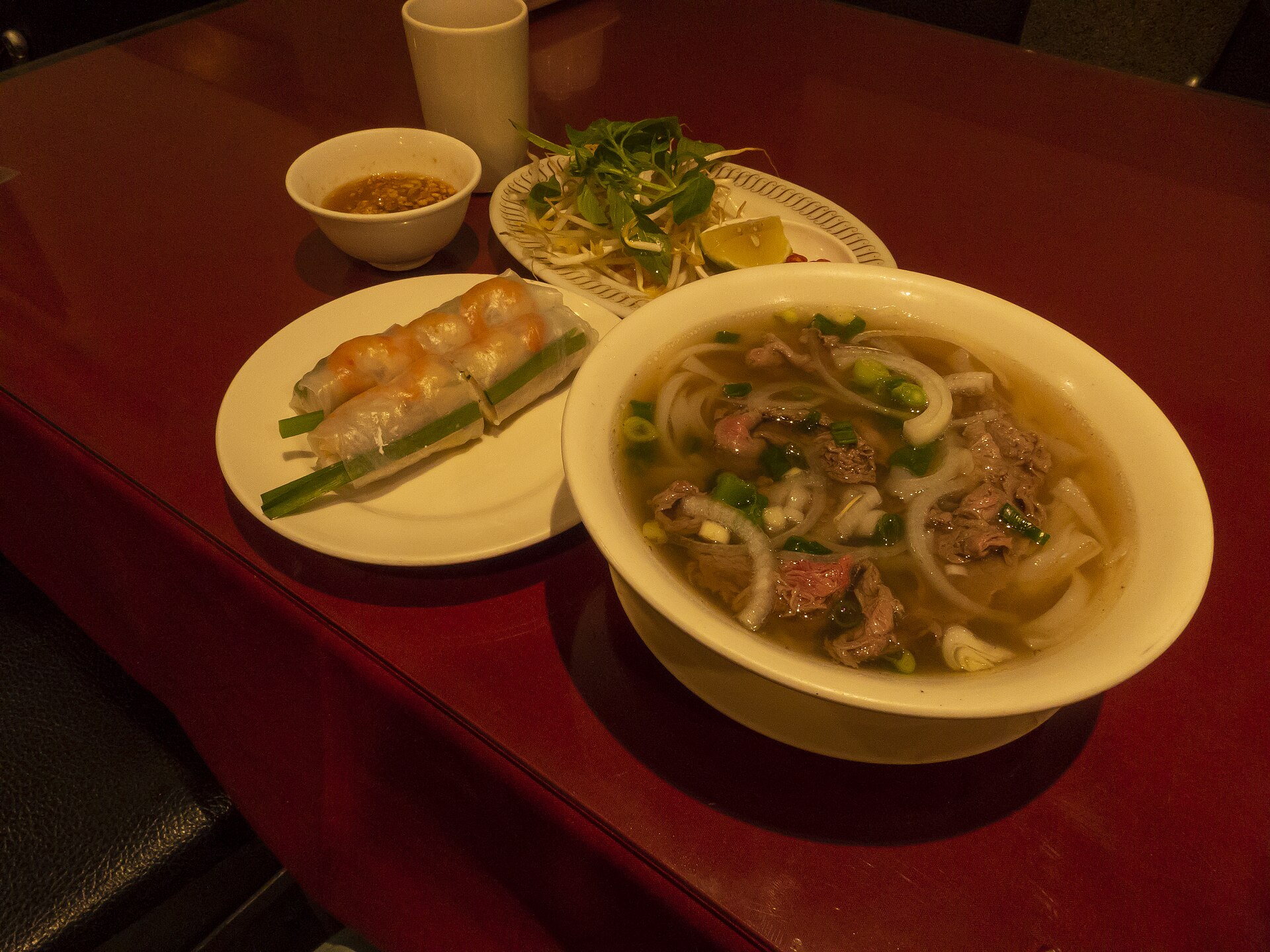Bàn ăn có phở bò, gỏi cuốn, rau thơm và nước chấm